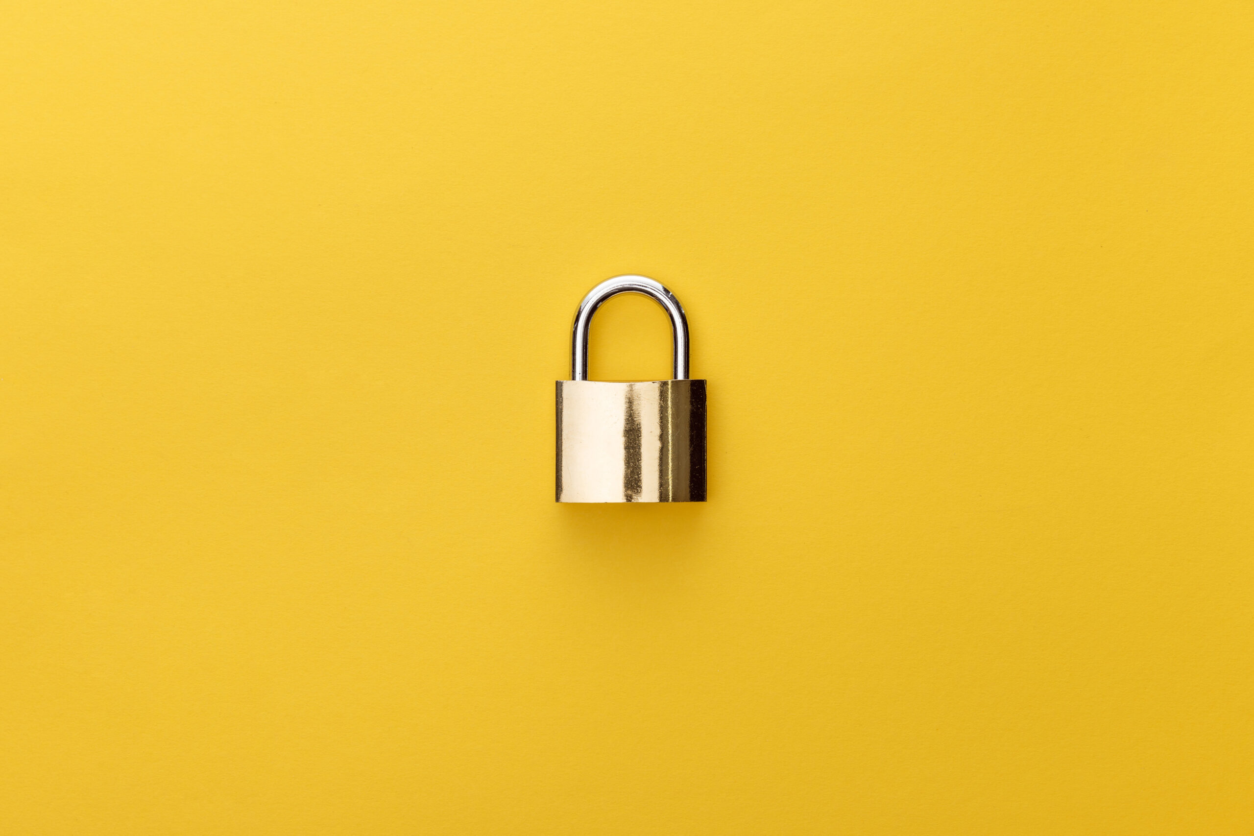 A metal pad lock in front of a yellow background.