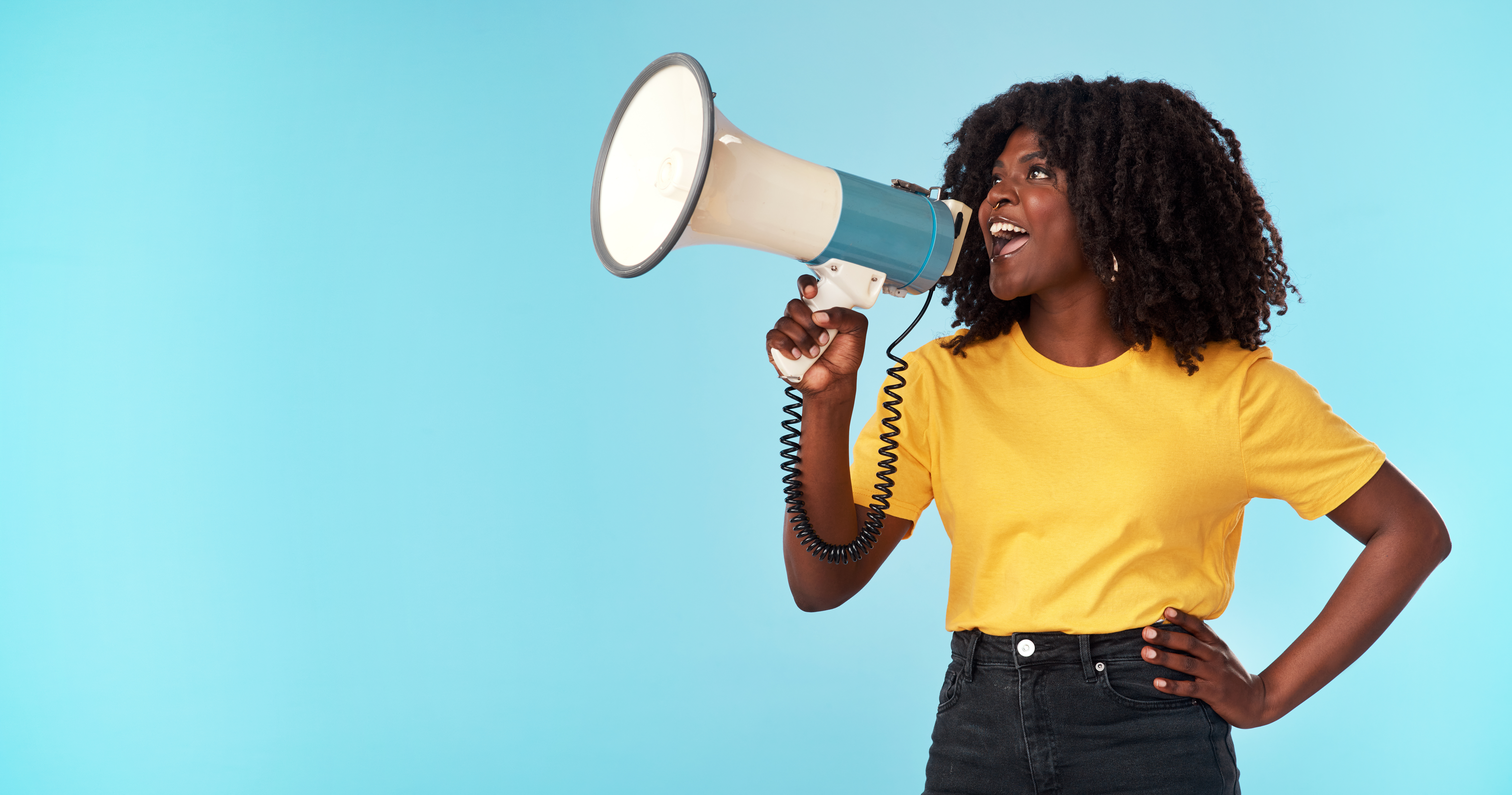 A woman talks into a megaphone in front of a light blue background.