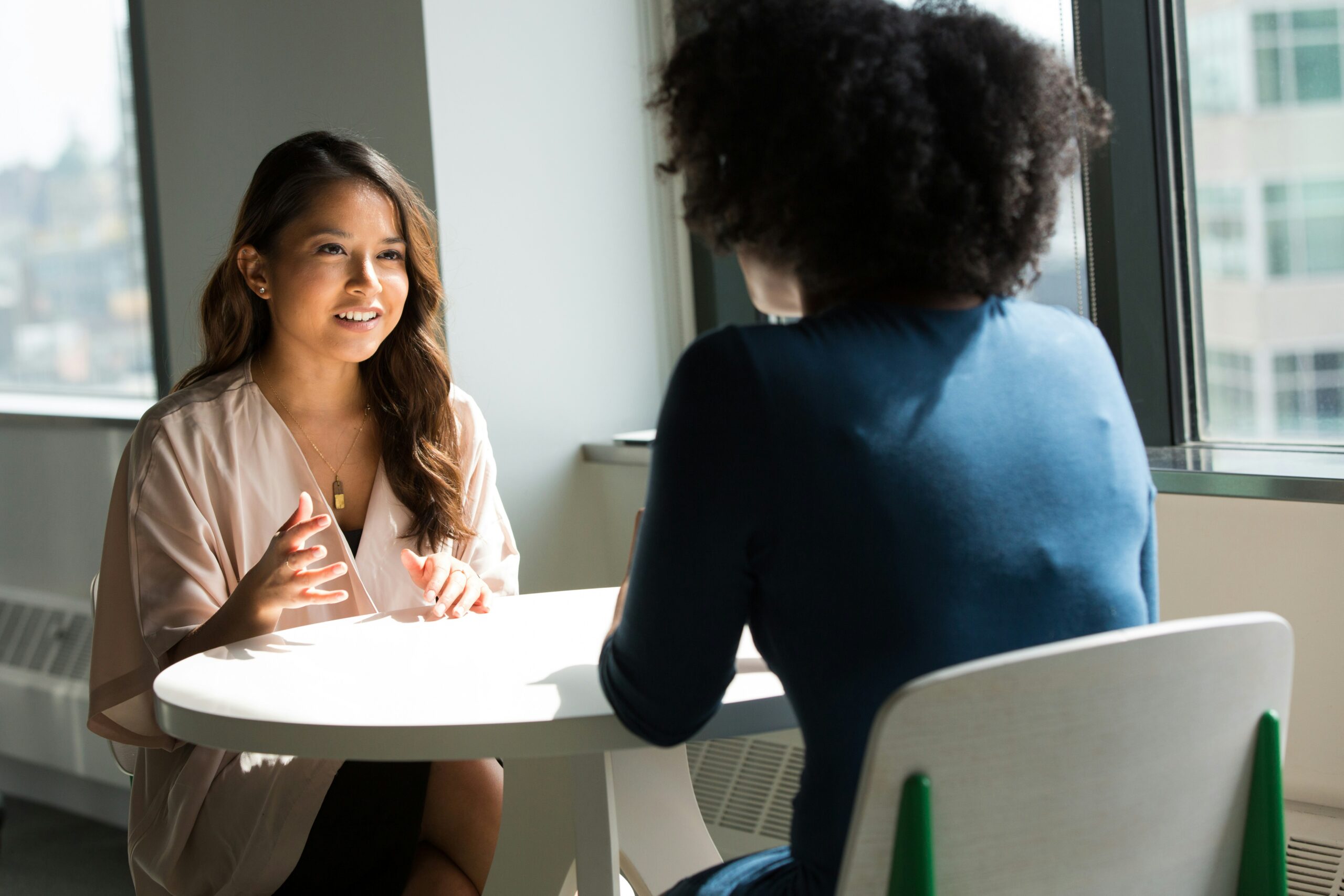 Two professionals engage in conversation while seated across from one another at a table.