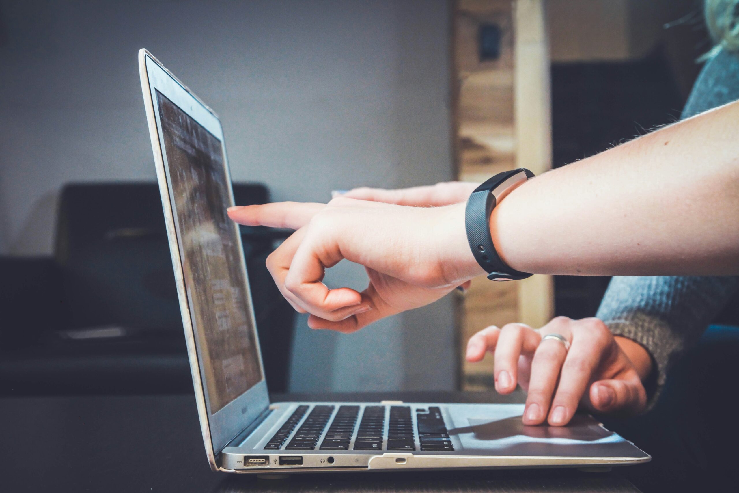 A hand points at the screen of a laptop while the other moves the mouse using the trackpad.