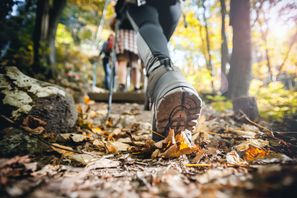 Hiker woman with trekking sticks climbs steep on mountain trail, focus on boot